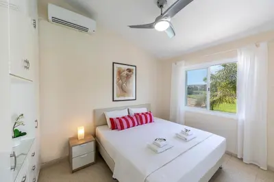 a bedroom with a white bed with red pillows and a window at Cape Greco Palm Trees Villa in Ayia Napa