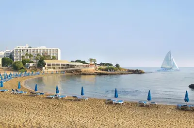 a beach with chairs and umbrellas and a sail boat at Villa Queen Alexandra in Protaras