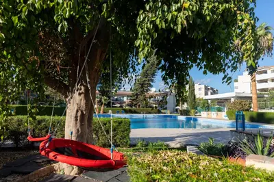 a red hammock hanging from a tree next to a pool at Palm Beach Apartment by TrulyCyprus in Limassol
