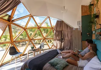 two women sitting on a bed in a room with a large window at Amazing Cyprus Glamping Domes - Glamping Cyprus in Paphos City