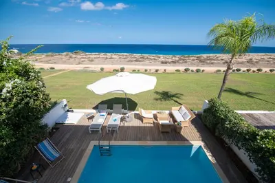 a swimming pool with chairs and an umbrella and the ocean at Jasmine Sea Front Villa in Protaras