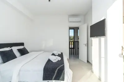 a white bedroom with a bed and a flat screen tv at Tsiolakki Homes Luxury Villas in Protaras