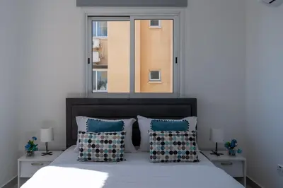 a bedroom with a bed with blue pillows and a window at Andrea 3-Bedroom Apt in Mackenzie in Larnaka